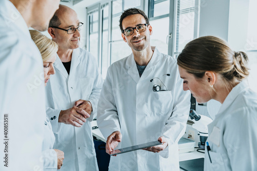 Smiling scientist holding digital tablet while standing by coworkers at laboratory photo