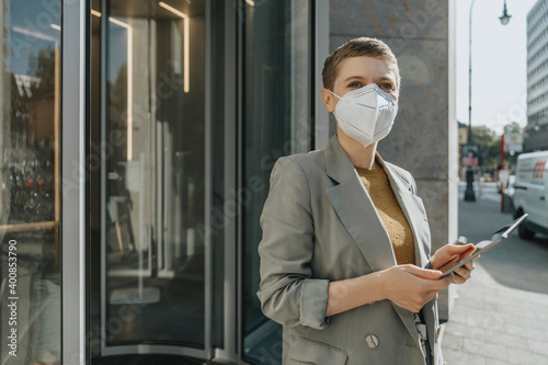 Woman wearing protective face mask using digital tablet while standing on street in city
