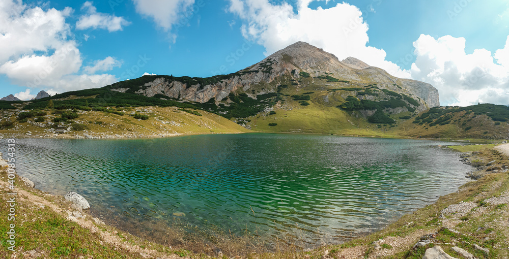 A panoramic view on the Le de Limo in Italian Dolomites. The lake has many shades, from turquoise to navy blue. High mountain behind it. High Alpine lake. Wandering and discovering remote places A panoramic view on the Le de Limo in Italian Dolomites. The lake has many shades, from turquoise to navy blue. High mountain behind it. High Alpine lake. Wandering and discovering remote places