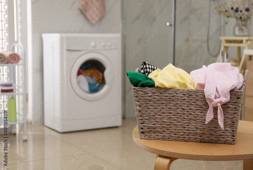 Wicker laundry basket full of different clothes on table in bathroom Wicker laundry basket full of different clothes on table in bathroom