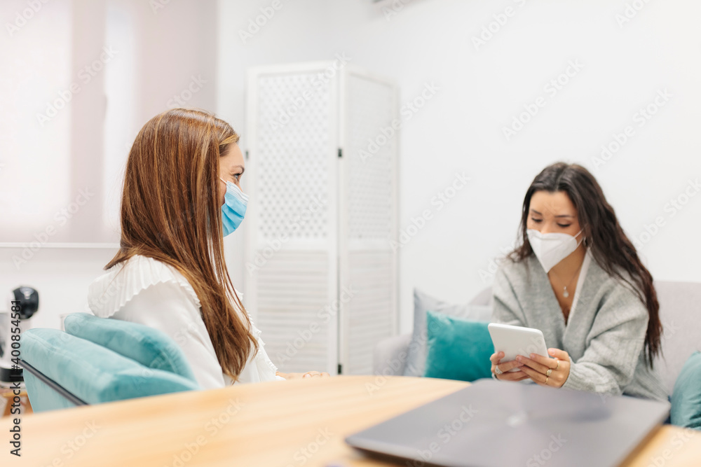 Patient wearing face mask using digital tablet while sitting by psychologist at office Patient wearing face mask using digital tablet while sitting by psychologist at office