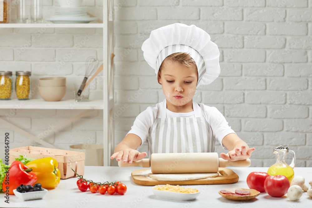 little child boy in chef hat and an apron roll a dough for pizza in the kitchen little child boy in chef hat and an apron roll a dough for pizza in the kitchen