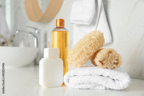 Natural loofah sponges, towel and cosmetic products on table in bathroom photo