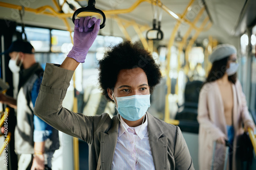 African American businesswoman wearing protective face mask and gloves while commuting to work by bus.