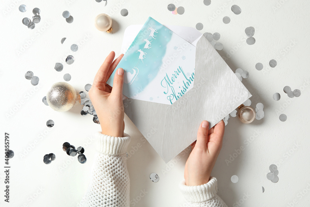 Woman taking greeting card with text Merry Christmas from envelope at white table, top view Woman taking greeting card with text Merry Christmas from envelope at white table, top view