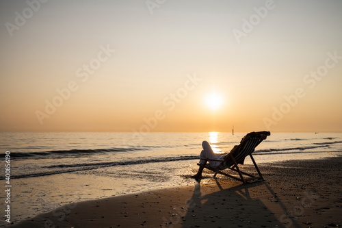 Young woman relaxing while sitting on folding chair at beach against clear sky during sunset