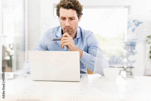 Mid adult man concentrating while working on laptop in office