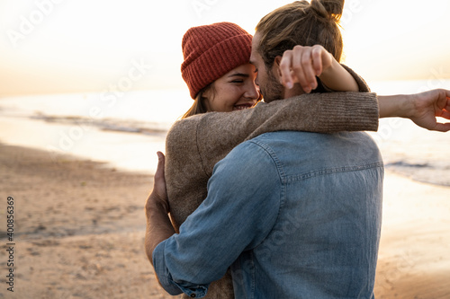 Smiling young woman embracing boyfriend while standing at beach during sunset