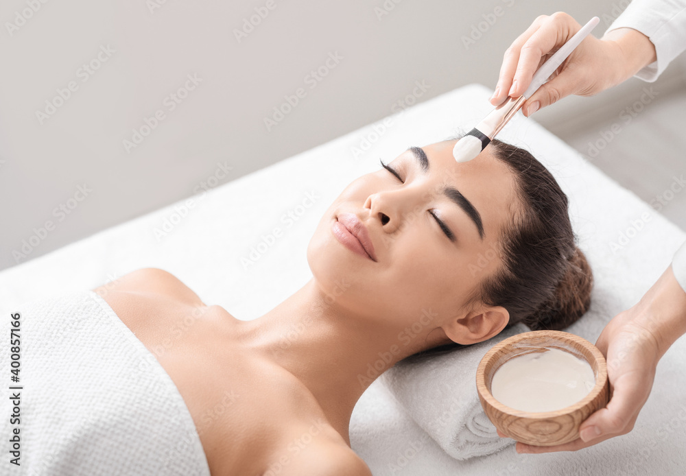 Beauty Treatment. Beautician applying clay mask to asian woman at spa salon