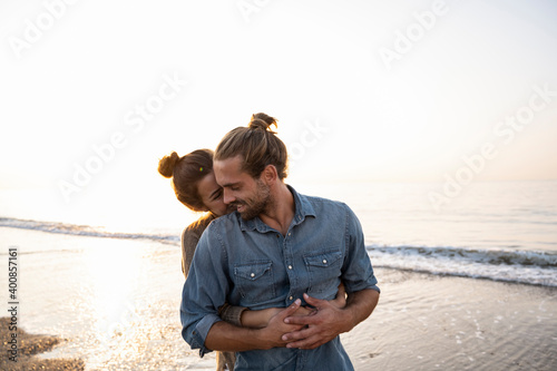 Woman embracing boyfriend from behind at beach against clear sky during sunset