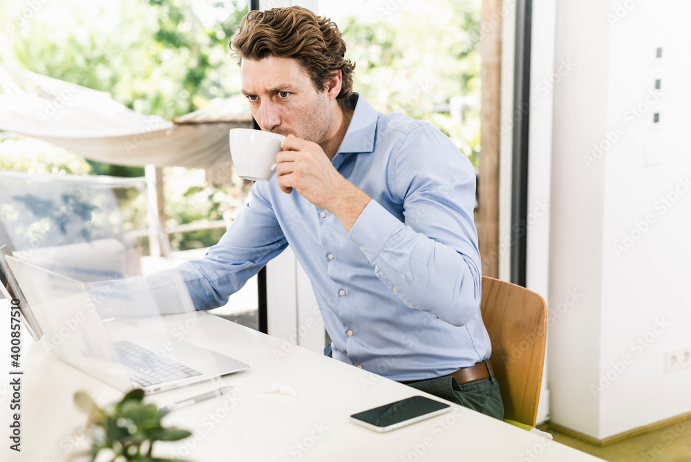 Man working on laptop while drinking coffee sitting in office Man working on laptop while drinking coffee sitting in office