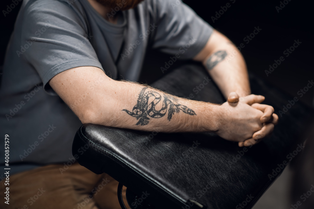 Close-up of a man's hands with a snake tattoo on a leather tattoo table in a tattoo parlor