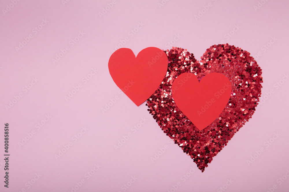 Heart shape made of red glitter and two paper handmade heart on pink background. Love concept.