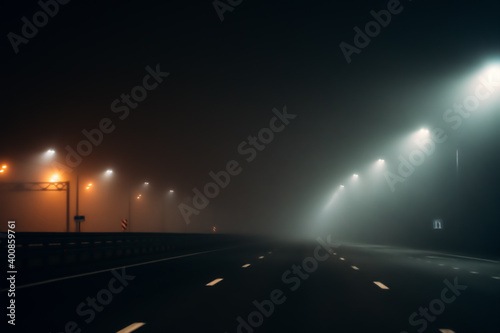Empty illuminated by city lamps foggy road at night in misty weather.