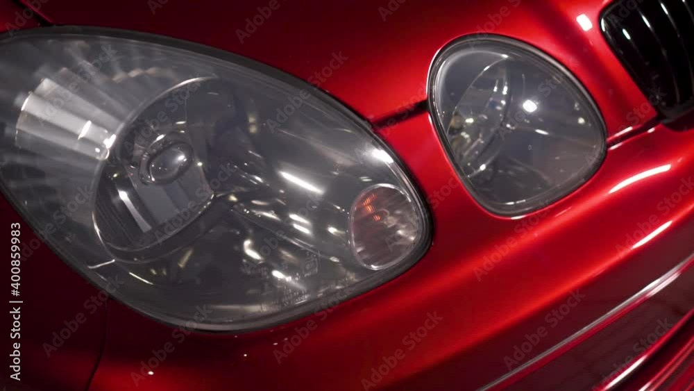 Close up view of car headlamp of car. Footage. Red spotrs auto hood, glass headlamp. Slow camera rotation.