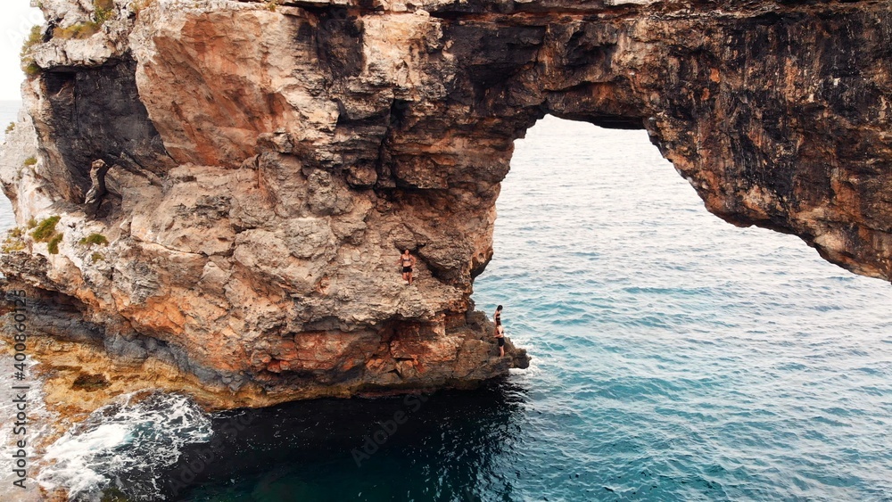 Es Pontas, turist climbling on Natural Rock Arch At The Coast Of Majorca Island, between Cala Santanyi and Cala Llombards, Spain. High quality photo
