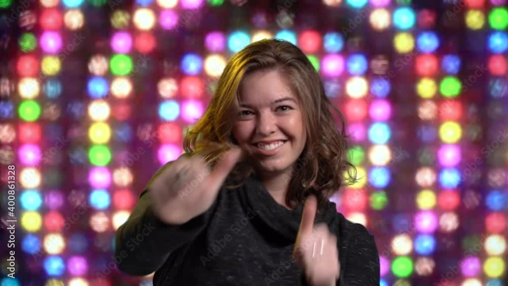 Cute woman dances pointing and thumbs up colorful lighted wall background Cute woman dances pointing and thumbs up colorful lighted wall background