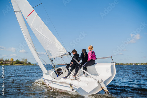 A fast, sporty, single-masted yacht with three athletes on board sails with a fair wind on a beautiful river