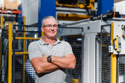 Confident male engineer with arms crossed standing in factory photo