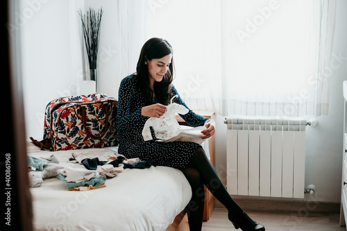 Pregnant woman folding baby clothes in bedroom at home photo