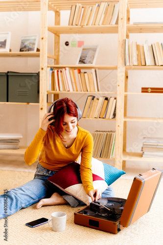 Smiling woman wearing headphones while using turntable sitting at home photo