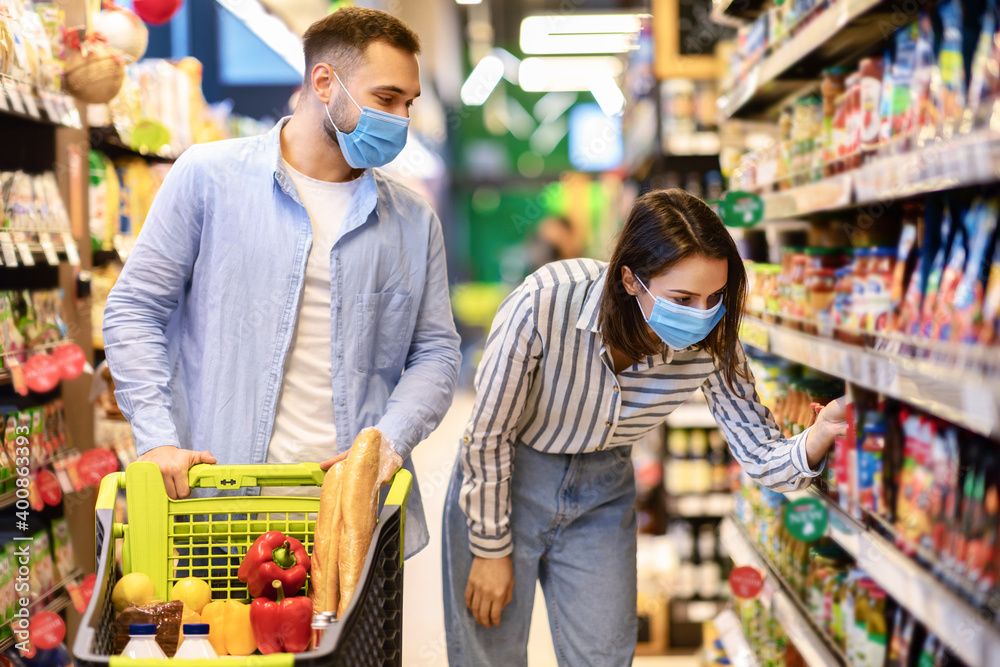 Young couple in face masks shopping in supermarket