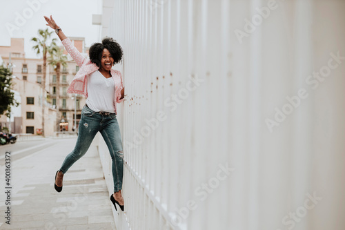 Cheerful woman with hand raised standing on fence in city