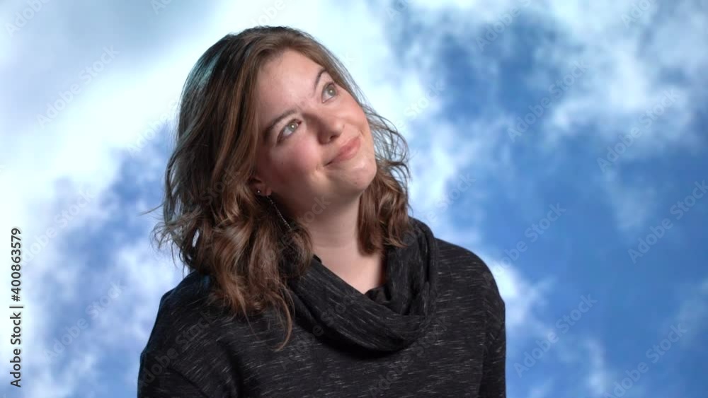 Beautiful young woman day dreaming in front of clouds slow motion Beautiful young woman day dreaming in front of clouds slow motion