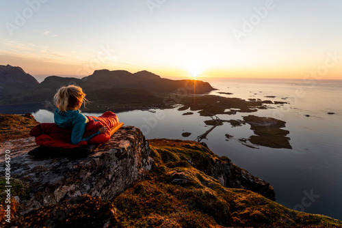 Hiker admiring sunset view while lying in sleeping bag at Volandstinden, Lofoten