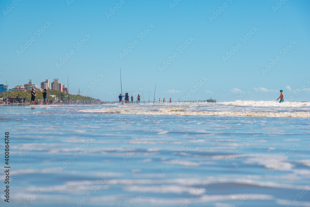 Mar del Tuyú, Buenos Aires, Argentina; December 06, 2020: View of the beach with a lot of fishermen and a pier in the background from inside the water