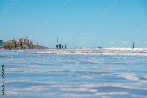 Mar del Tuyú, Buenos Aires, Argentina; December 06, 2020: View of the beach with a lot of fishermen and a pier in the background from inside the water