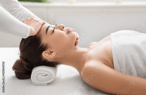 Professional therapist making relaxing head and face massage for young asian lady