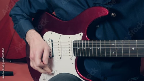 Man in a blue shirt plays a red electric guitar. The hand of man has smoothly over the strings and switches the lever of the pickups. Close up shot photo