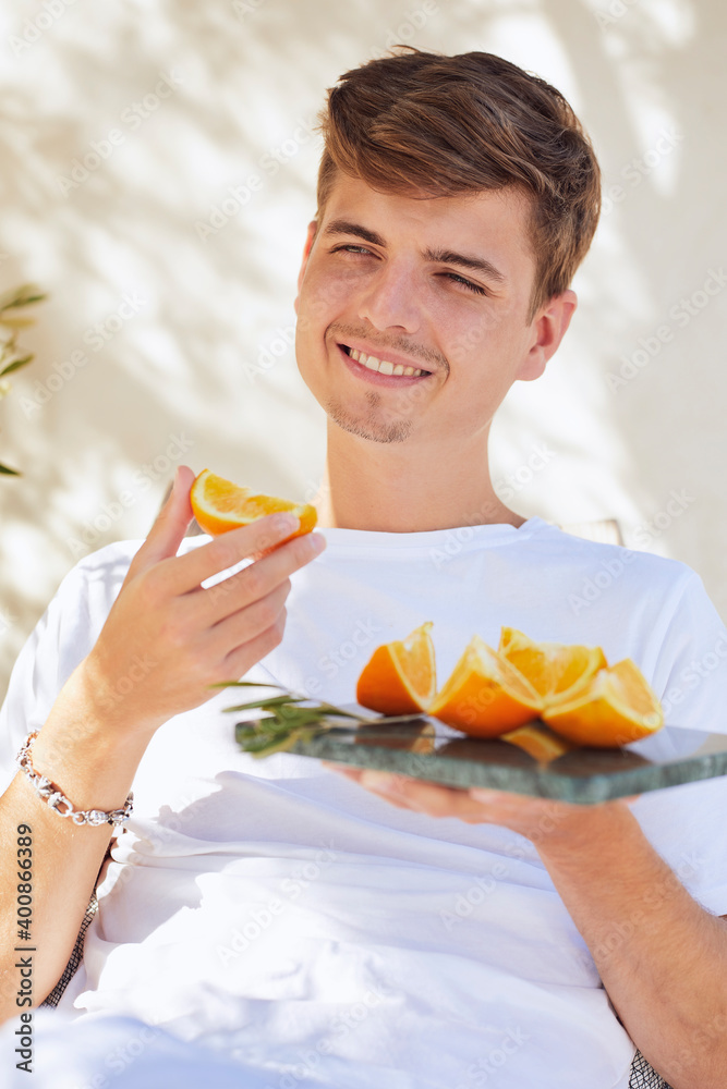 Smiling young man holding slice of oranges against wall Smiling young man holding slice of oranges against wall