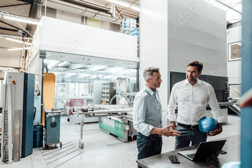 Male engineers discussing over laptop in manufacturing industry photo