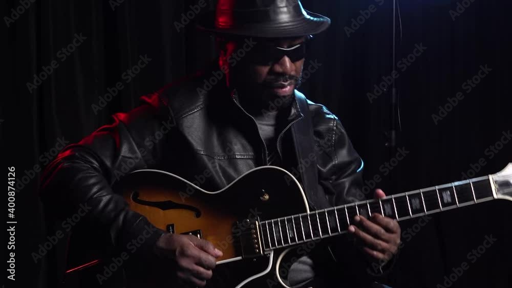 Jazz guitarist in leather hat dark glasses strumming strings close up
