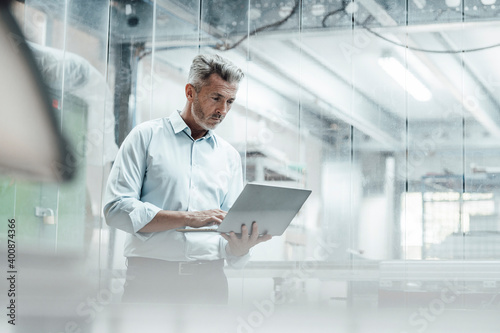 Thoughtful male engineer using laptop while standing in industry photo