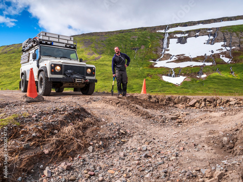 Man leaning on shovel in front of pot hole in middle of dirt road leading to Drangajokull photo