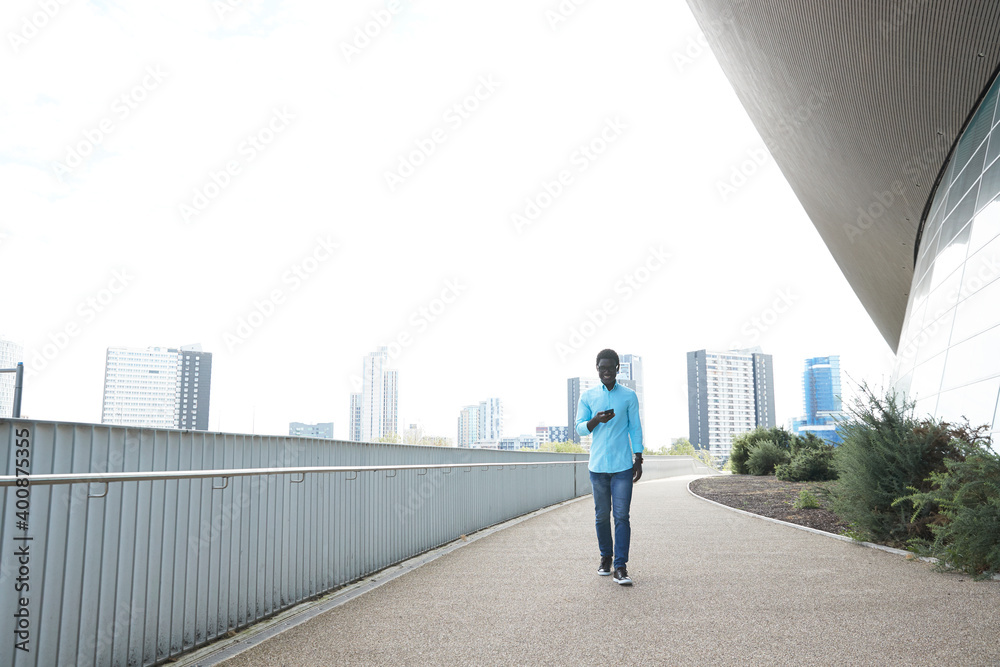 Smiling man using smart phone while walking on footpath in city Smiling man using smart phone while walking on footpath in city