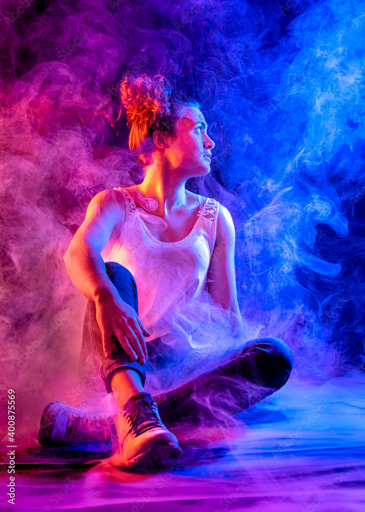 Young woman looking away while sitting amidst pink and blue smoke at studio Young woman looking away while sitting amidst pink and blue smoke at studio