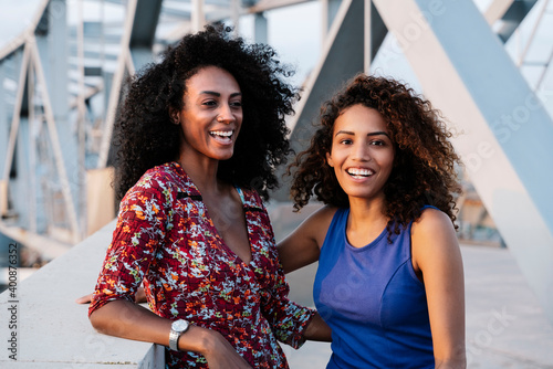 Happy young female friends by retaining wall on bridge