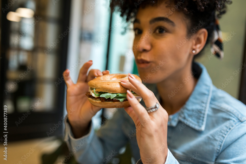 Mid adult woman eating burger while sitting at cafe Mid adult woman eating burger while sitting at cafe