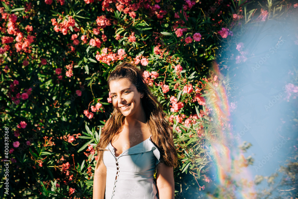Smiling young woman with long hair standing against plants in park on sunny day
