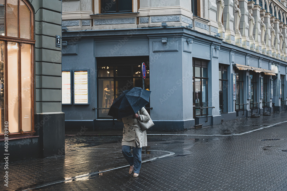 A single woman walks in the old city with an umbrella in the rain and wind.