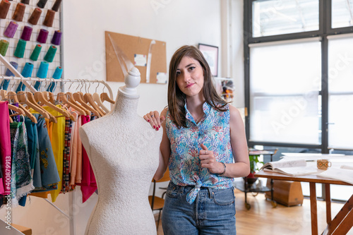 Confident young female fashion trainee standing by dressmaker's dummy at design studio photo