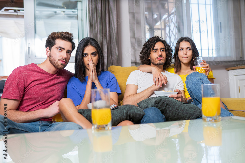 Young multi-ethnic friends in stress watching TV at home