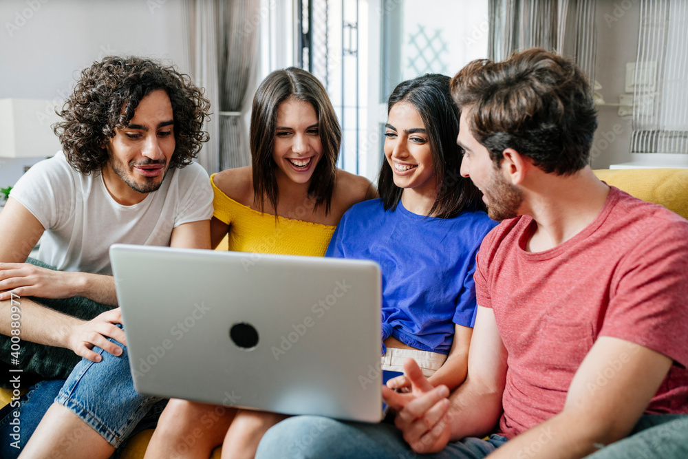 Smiling multi-ethnic friends sharing laptop while sitting in living room