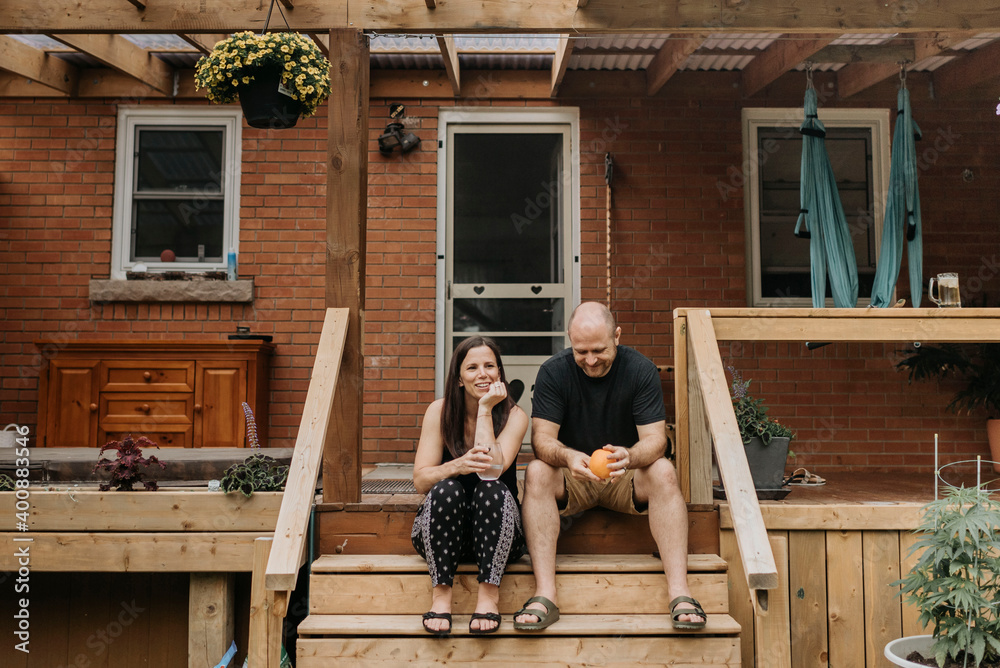 Couple holding drinks talking while sitting on steps outside house Couple holding drinks talking while sitting on steps outside house