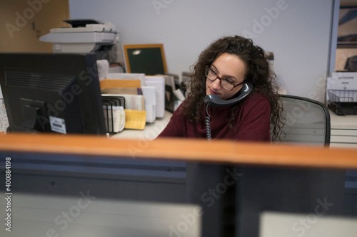 Young woman in cubicle talking via telephone