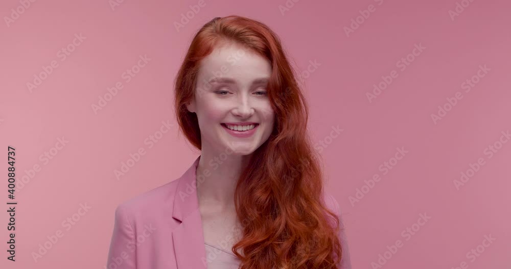 Beautiful female Model posing on Camera, standing in the Foreground, enjoying her Job. Looking Pretty and Stylish, wearing trendy Pink Jacket. Pink wall in the Background. Charming red hairstyle. Beautiful female Model posing on Camera, standing in the Foreground, enjoying her Job. Looking Pretty and Stylish, wearing trendy Pink Jacket. Pink wall in the Background. Charming red hairstyle.